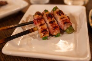 Three bacon-wrapped asparagus skewers on a white plate.